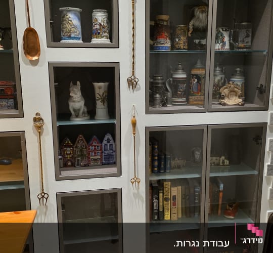 ספריית קיר בנויה מעץ עם דלתות זכוכית ומדפים לתצוגת חפצי נוי וספרים